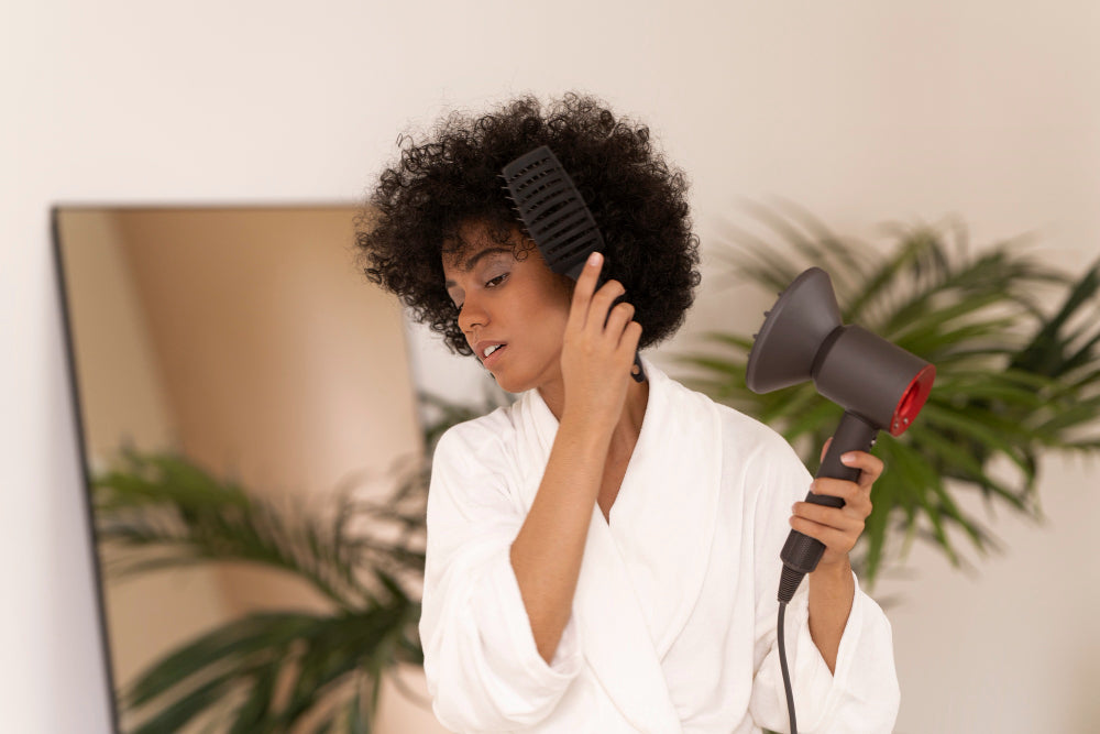 Femme séchant ses cheveux crépus au sèche-cheveux avec une brosse