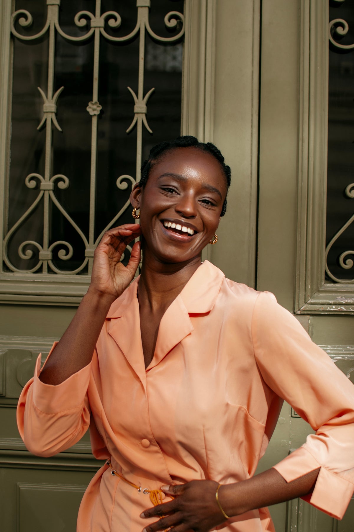 Femme souriante aux cheveux crépus plaqués devant une porte ancienne