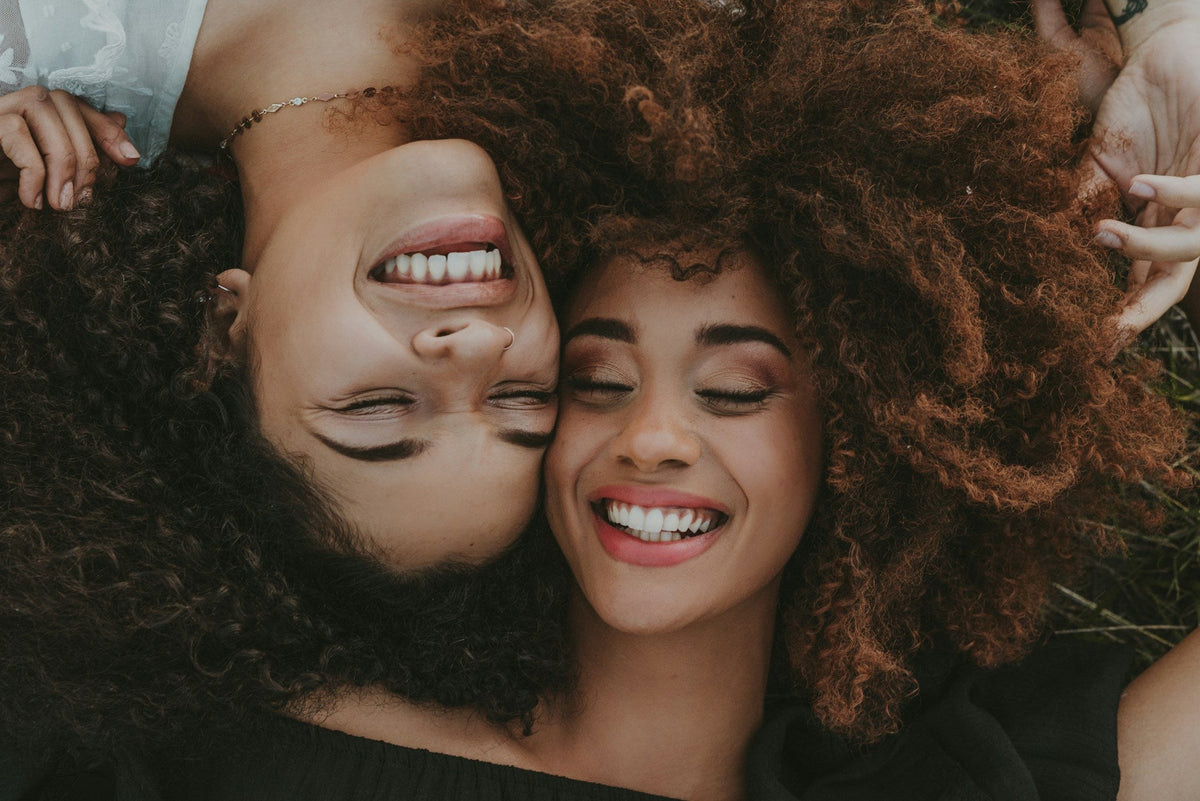 Deux femmes souriantes allongées, leurs cheveux bouclés déployés