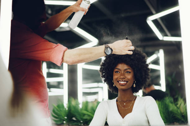 Coiffeuse vaporisant un soin sur les cheveux crépus d'une cliente en salon