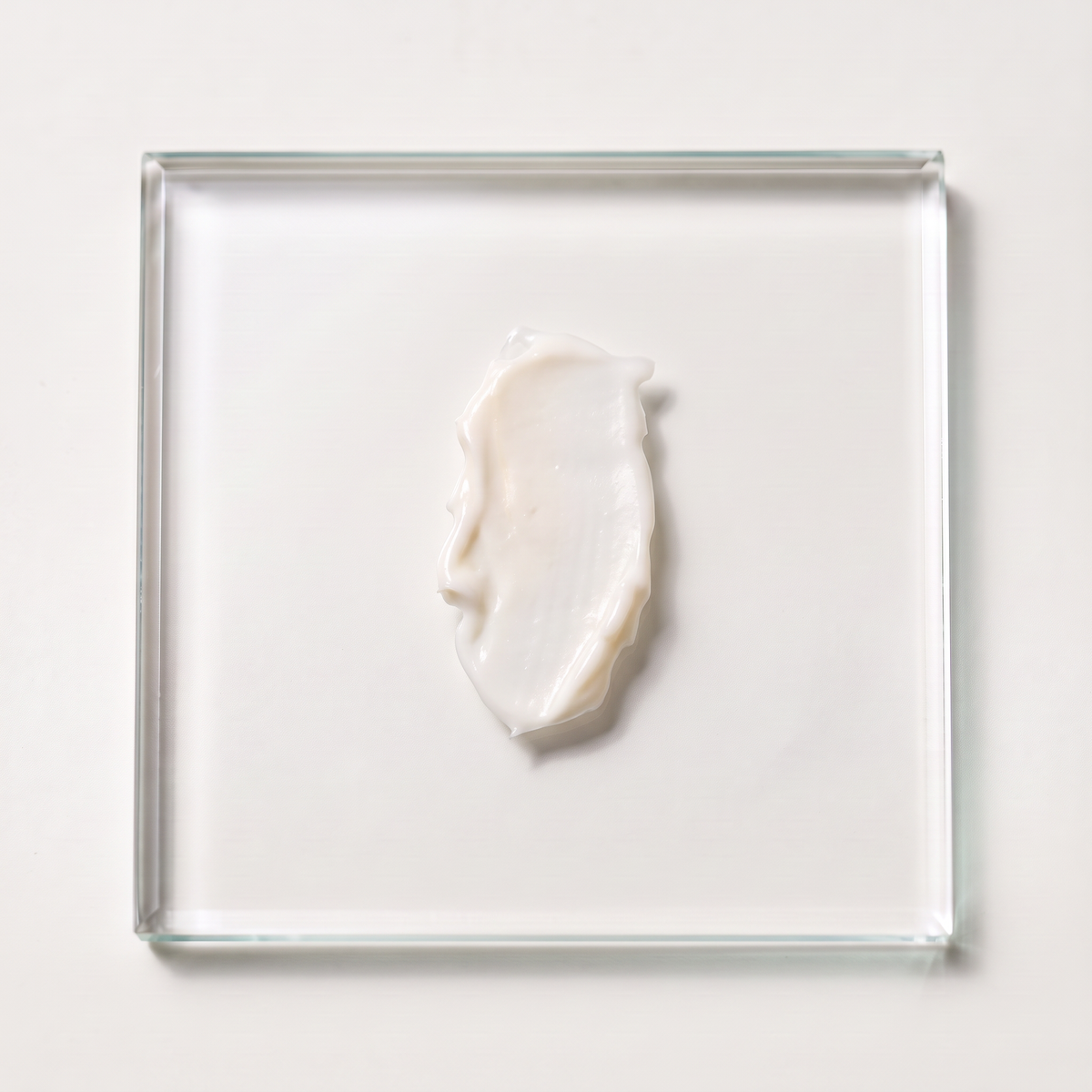 Texture blanche de La Crème Coiffante étalée sur un carré de verre