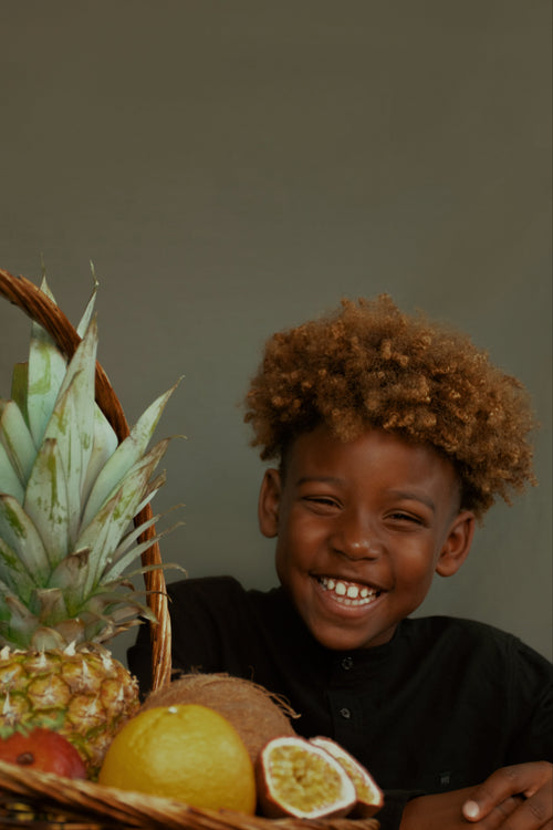 enfant roux noire souriant cheveux crepus devant des fruits