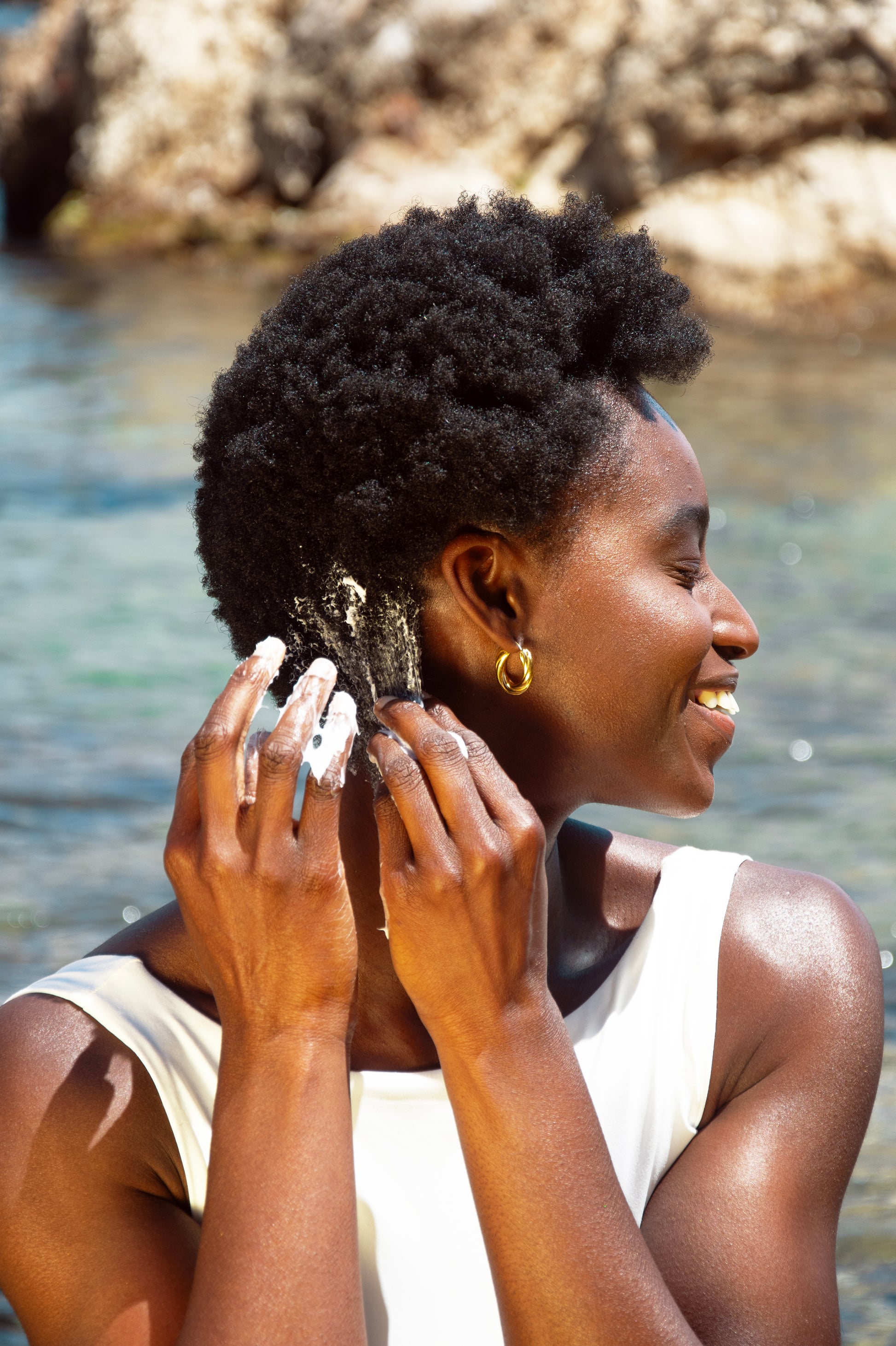 femme noire cheveux crépus se coiffant avec crème maillot de bain blanc à la plage creole doree
