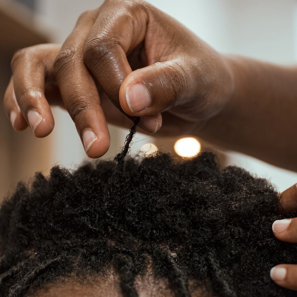 Gros plan sur les mains d'une coiffeuse séparant une section de cheveux crépus